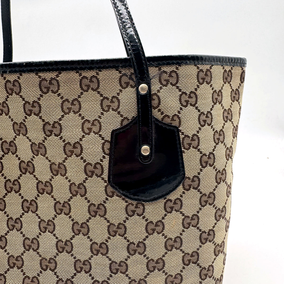 Gucci Tote Toile GG Beige et Cuir Verni Noir - détail de l'attache d'anse et de la patte vernie